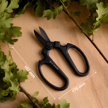 將圖片載入圖庫檢視器 Black pruning shears on a wooden surface with green leaves
